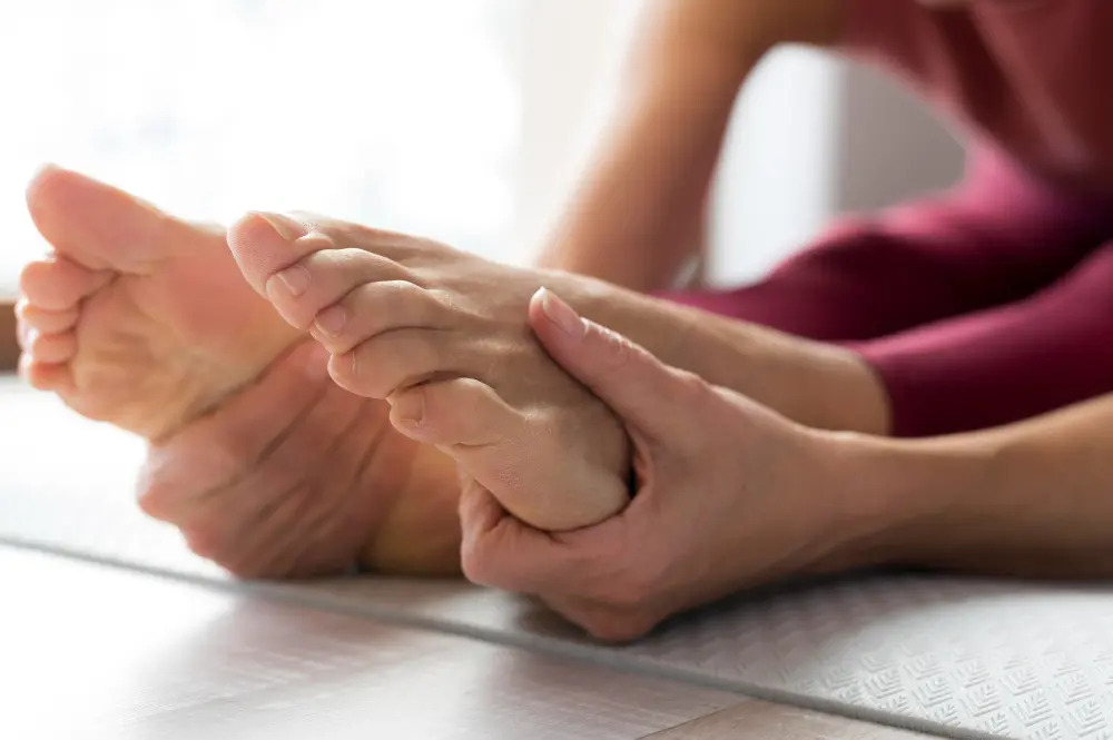 Close-up of a person’s hands gently holding and stretching their foot on a yoga mat while wearing activewear, helping relieve numbness and tingling.