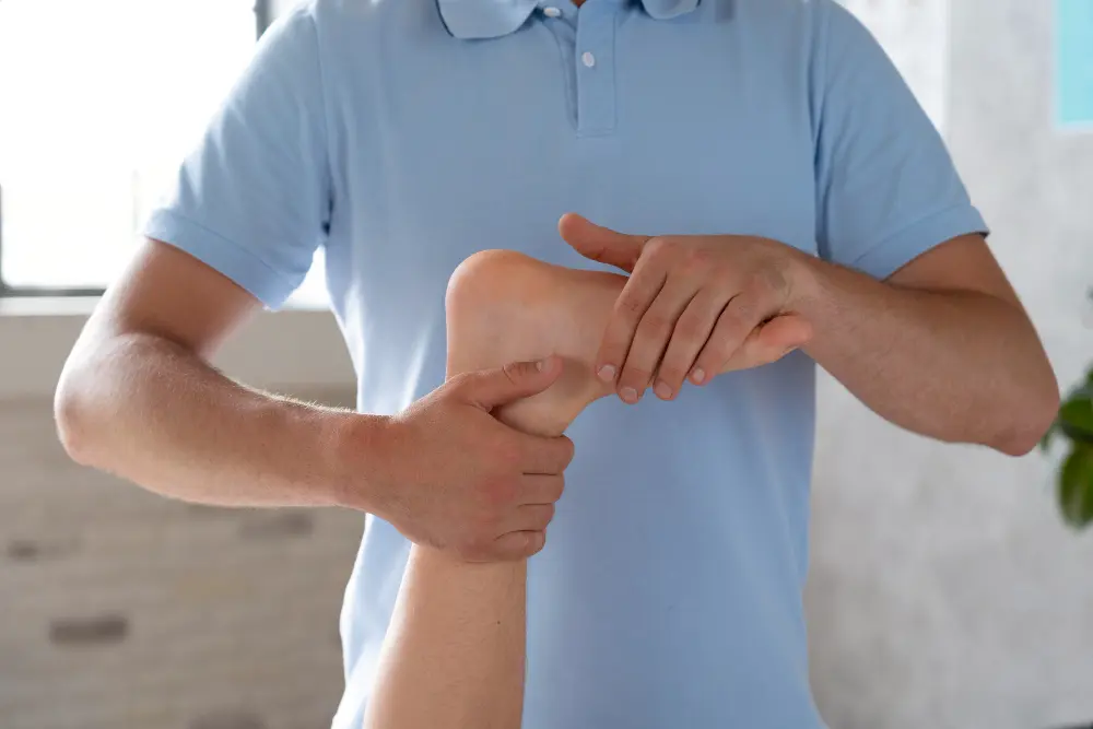 Close-up of a therapist in a blue polo shirt manipulating a patient’s bare foot and ankle with both hands, providing therapy for a possible pinched nerve.