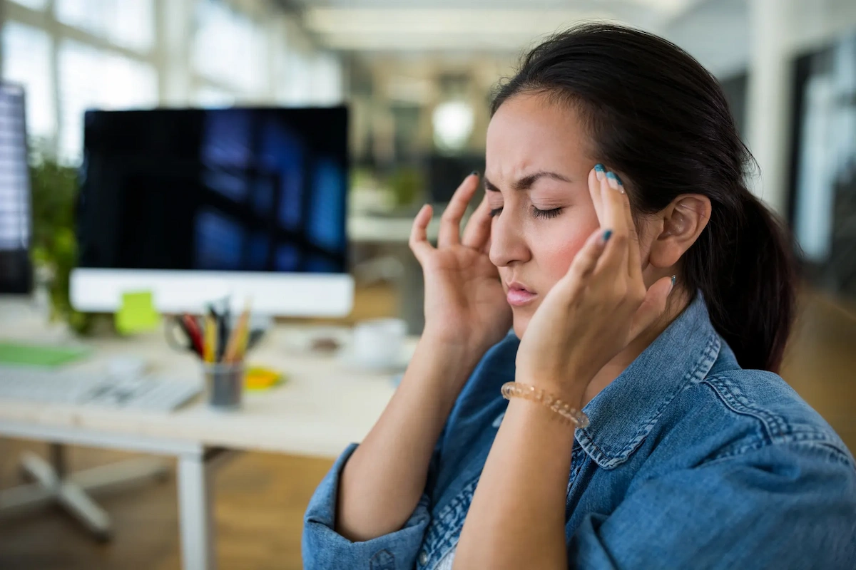 Woman pressing her temples with eyes closed, showing signs of headache or migraine pain