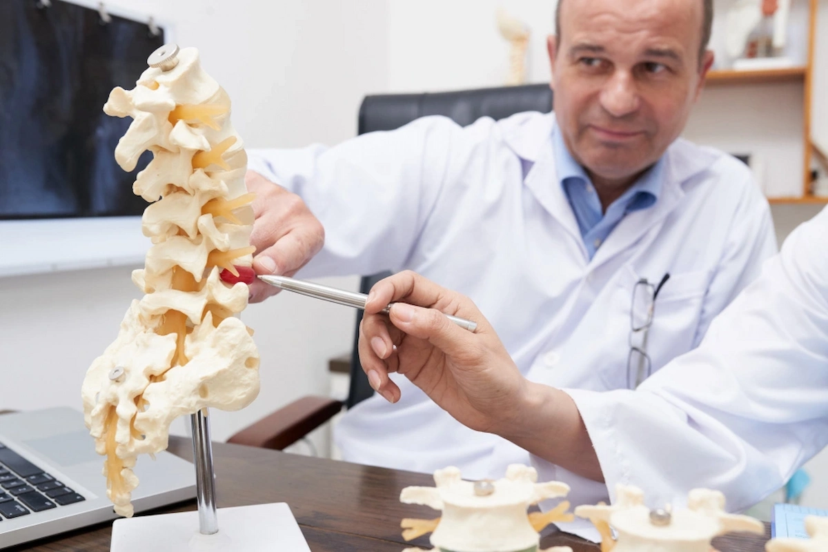 Doctor explaining a herniated disc using a spine model, highlighting the affected area