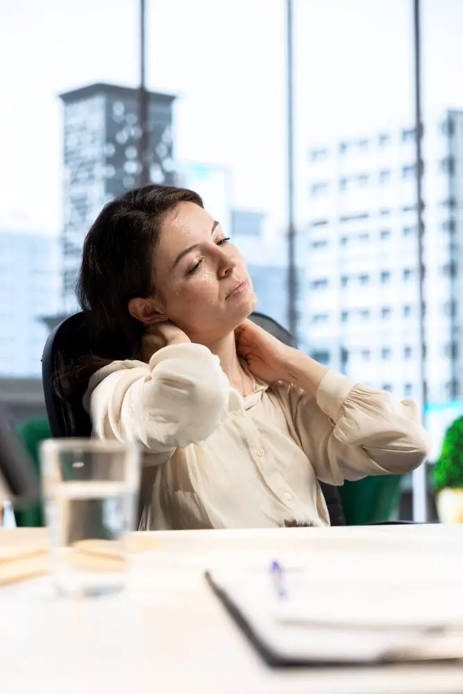 Woman sitting in office chair holding neck from whiplash pain.