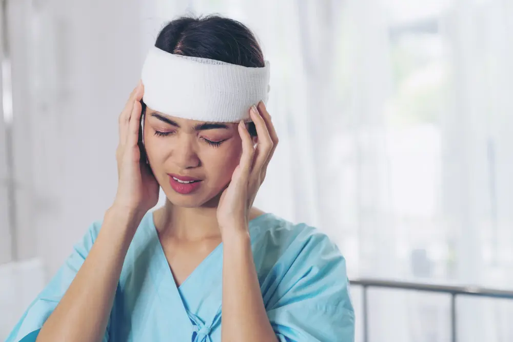 Young woman with a head bandage holding her temples due to whiplash and concussion pain.