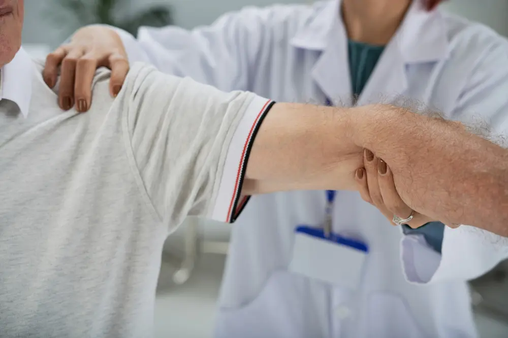 Close-up of a medical professional in a white lab coat examining a patient’s arm and shoulder, holding the arm and shoulder to assess a possible pinched nerve.